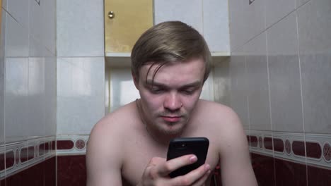 man using phone in a small bathroom toilet