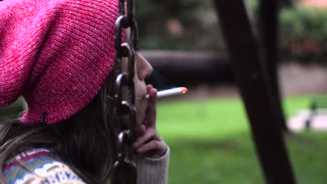 close up of a young woman smoking a cigarette in a swing