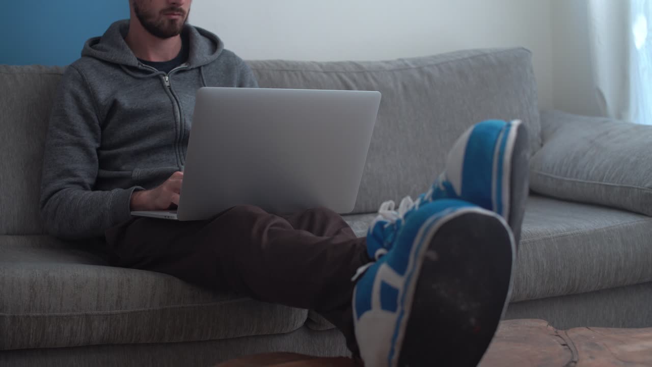 el hombre se sienta cómodamente en el sofá y trabaja en una laptop desde casa