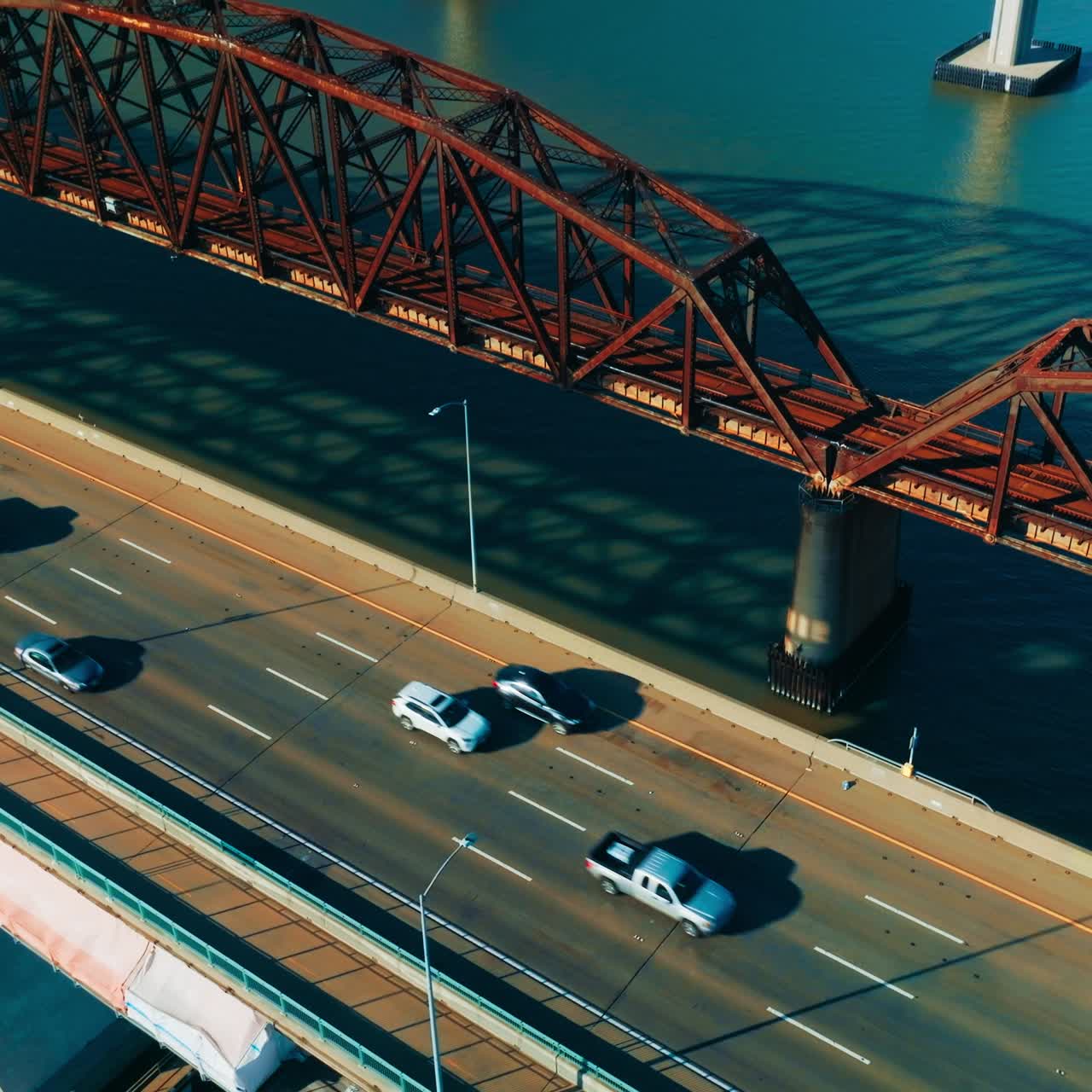 Bridge with four-lane one-way road. Quick cars moving by the highway. Metal rusty railway bridge beside. View from top