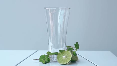 Glänzendes-Glas-Auf-Dem-Tisch-Neben-Limettenhälften-Und-Minzblättern