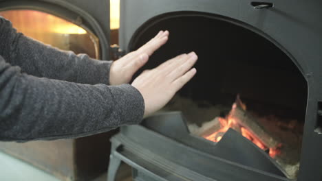 person warms hands near fire in  black metal fireplace. cozy home concept