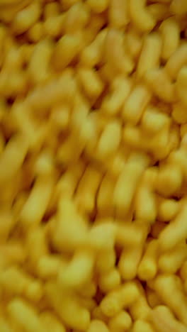 plenty of sweet corn snacks being mixed in metal tank. close up. manufacturing maize crispy sticks at factory. vertical video