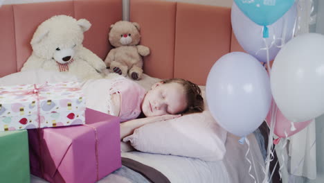 a child sleeps in his bed, next to gift boxes and balloons.