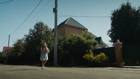little girl walks slowly along quiet suburban street under bright sunlight, holding toy in hand, surrounded by lush trees and houses, she moves through peaceful residential neighborhood