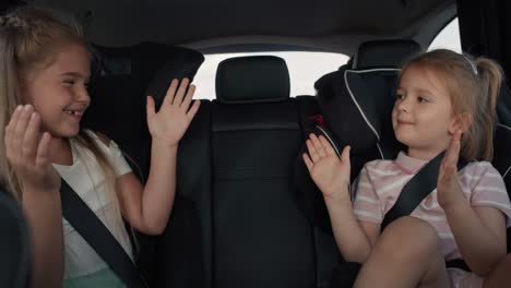 Two-caucasian-female-children-sitting-on-the-back-seat-and-playing-clapping-game.