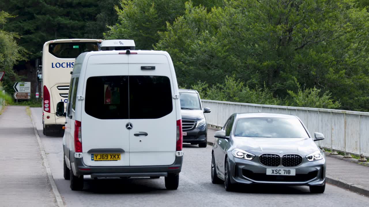Cars and vans carefully navigate a narrow bridge in the scenic Scottish Highlands