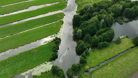 Aerial-rising-shot-of-a-boat-cruising-in-a-canal-among-numerous-slagenlandschap,-trees-and-fields-in-a-polder-in-the-Krimpenerwaard-region-of-the-Netherlands
