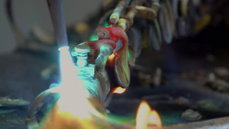 a blacksmith uses gas welding to melt a brass saxophone, resulting in destructive sparks and brightly coloured flames