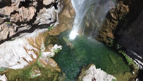 aerial view of a person swimming at the base of a majestic waterfall