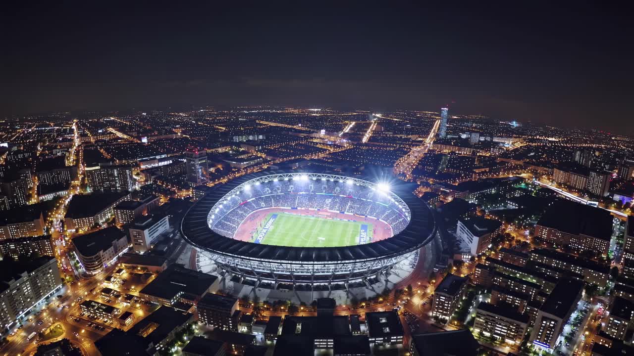 Aerial view of a brightly lit stadium at night, surrounded by city lights