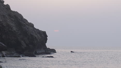 Dawn-at-cliffside-as-seagulls-fly-and-calm-sea-waves-wash-upon-shoreline