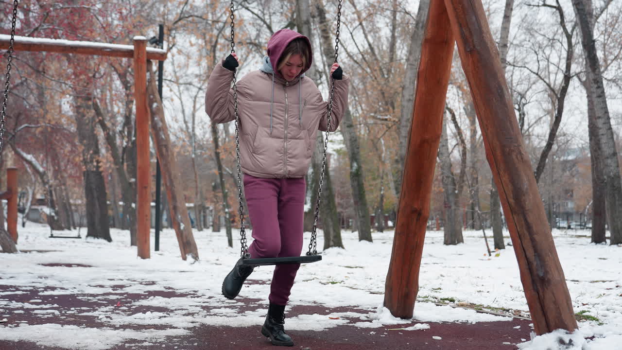 따뜻한 겨울 의상을 입은 젊은 여성은 눈 인 야외 공원에서 철의 스에 무을 고, 눈으로 인 땅과 벌거벗은 나무는 그녀가 스에 균형을 잡는 동안 차가운 분위기를 만니다.