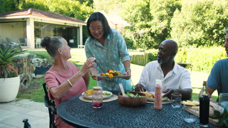 senior diverse couple enjoying in garden barbecue, serving colorful skewers and corn on table