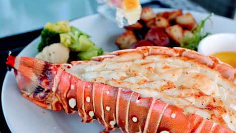 squeezing lime onto lobster tail with potatoes and butter, gourmet seafood plate