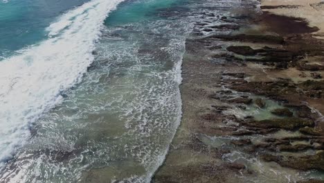 Volando-Sobre-Las-Olas-Rodando-Hacia-La-Costa-Rocosa,-Filmado-En-Uluwatu,-Bali,-Indonesia,-Playa-De-Arrecife-Tropical