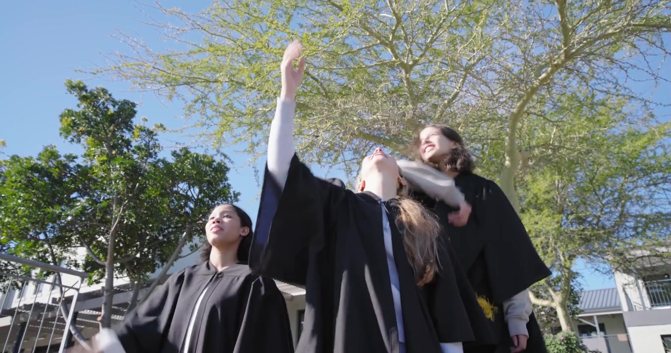 Laureate che sistemano i toques nelle toghe, camminano e lanciano i toques, si abbracciano e festeggiano nel campus