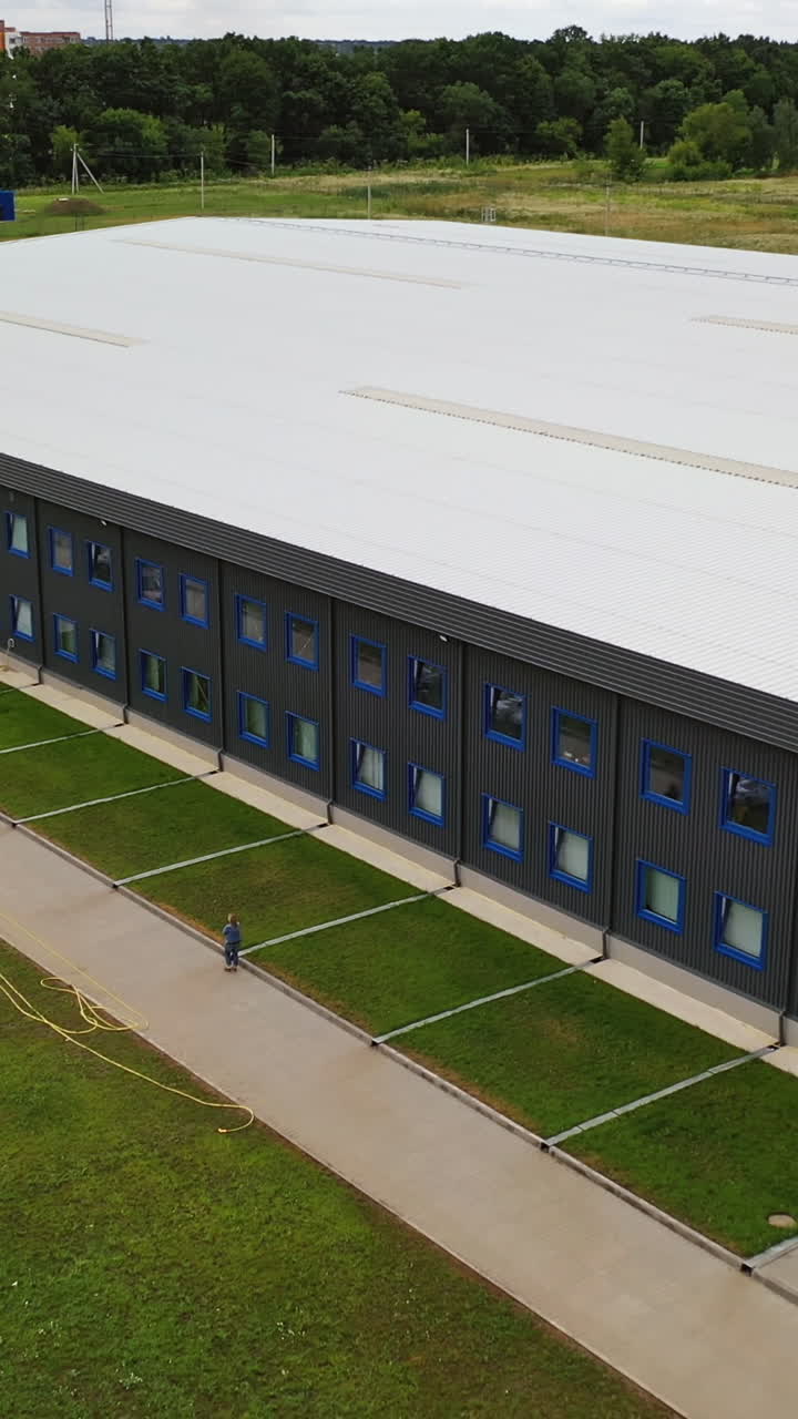 Facade of a modern two-storey building. Industrial plant outdoors. Aerial panorama of beautiful manufacturing with car parking. Summer time. Vertical video