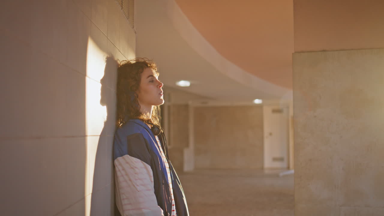 chica masticando apoyada en la pared edificio urbano bajo la luz del sol de la noche de cerca.