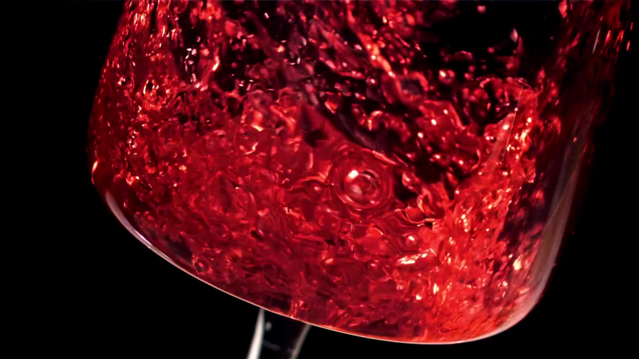 Vino rosso versato in un bicchiere su sfondo nero al rallentatore.