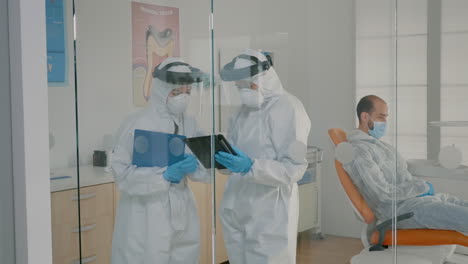 team of dentists with ppe suits holding tablet for teeth consultation