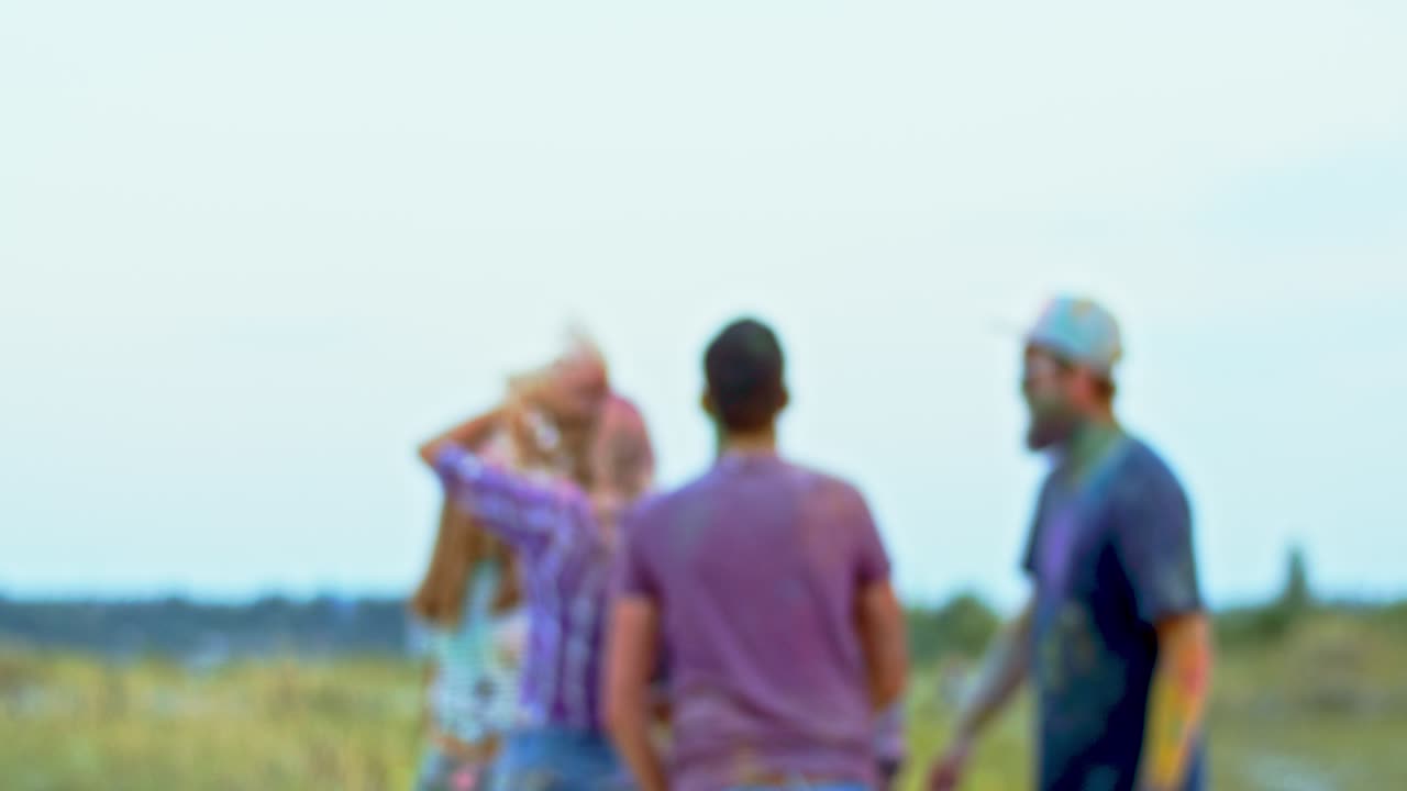 toma borrosa de los jóvenes bailando y divirtiéndose al aire libre en el festival holi, un joven apuesto que se acerca a la cámara, sonríe y posa para la cámara