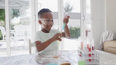 African-american-boy-sitting-at-table-holding-test-tubes-with-liquid,-in-slow-motion