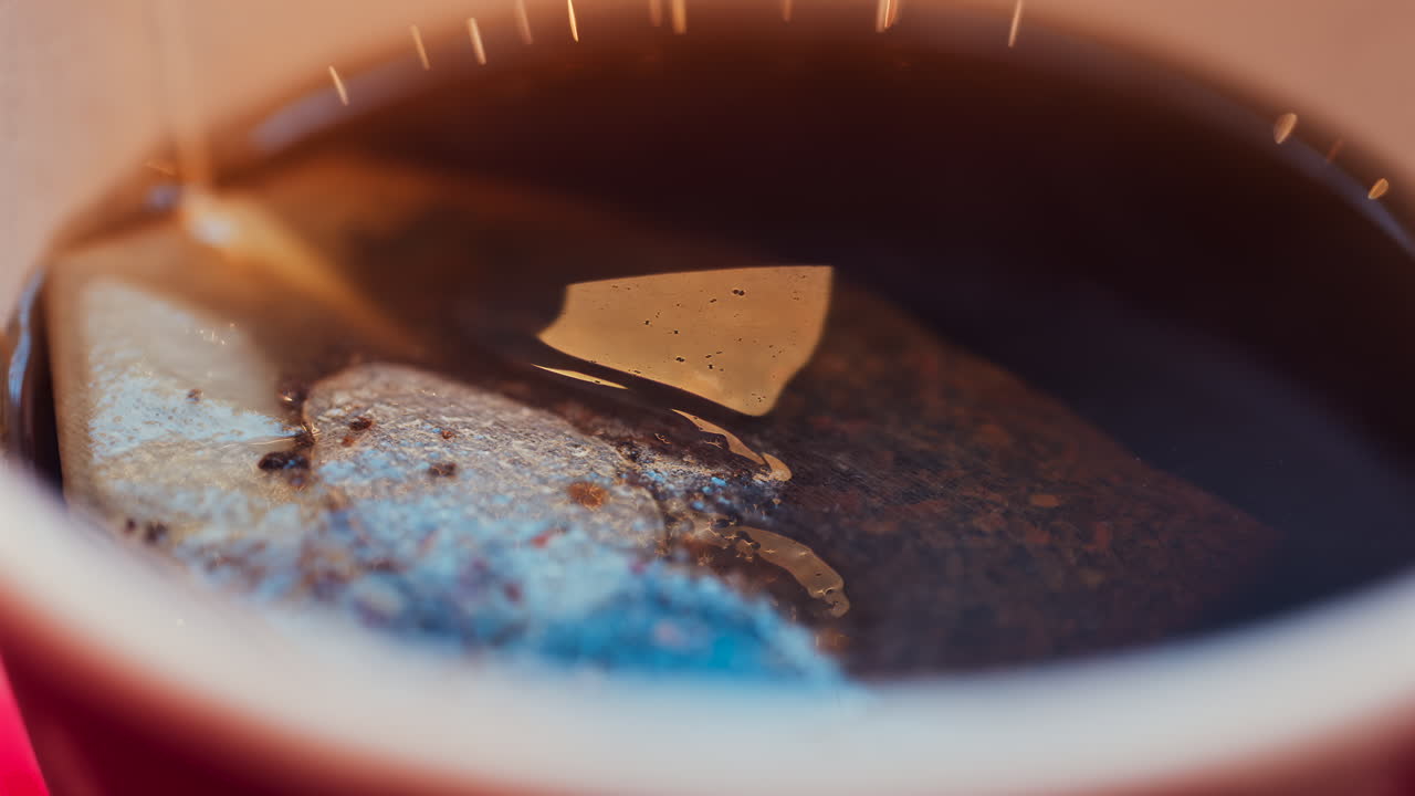 Close up of a tea bag brewing into a red cup