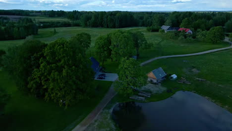 Aerial-Perspective-of-a-Wooden-House-Nestled-Amidst-Grass-Fields-and-Woodlands