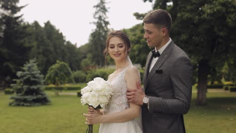 Newlyweds,-caucasian-groom-with-bride-walking,-embracing,-hugs-in-park,-wedding-couple