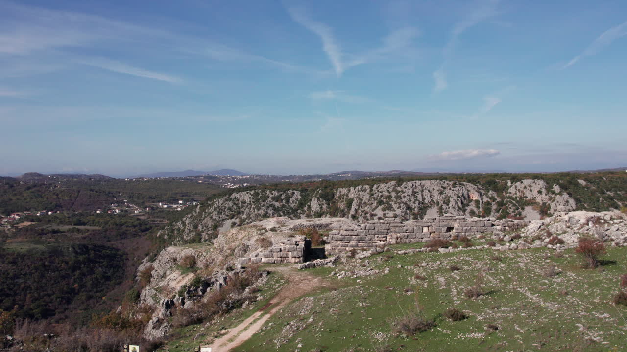 Aerial view of the ancient Daorson Illyrian fortress near Stolac, showing massive stone walls and a wide plateau surrounded by rugged hills and clear sky, captured in bright daylight