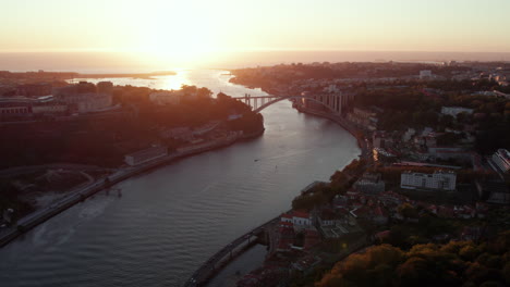 drone flyover view of river with bridge and city during sunset on horizon, porto, portugal