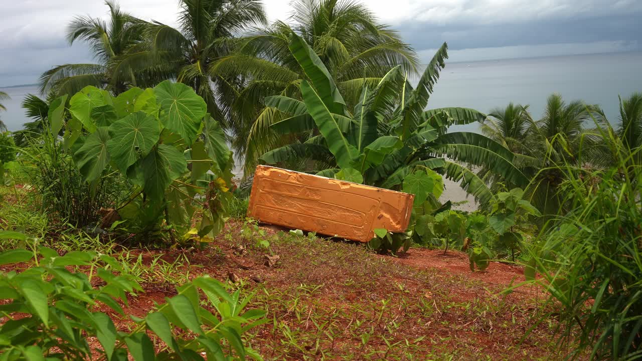 A wider shot of an orange styrofoam block on a red soil earth amid tropical growth, its presence a quiet marker of intrusion near Mauban Port, Quezon Province Philippines