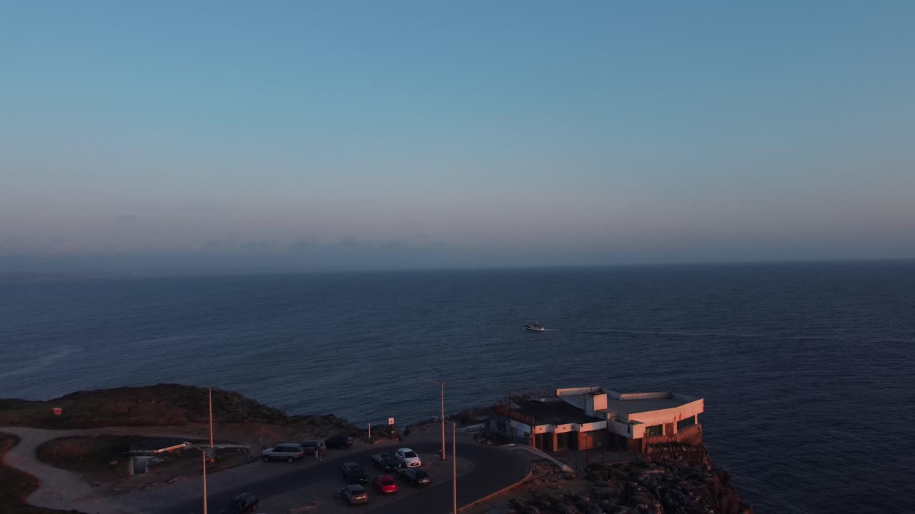 Dolly out shot of a cliff in peneche, portugal with a boat in its waters at dusk - aerial