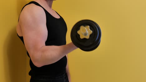 Unrecognizable man exercising with dumbbell doing bicep curls on yellow background.