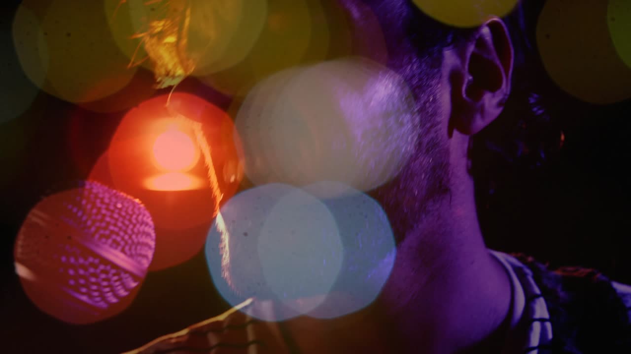 Male singer opening mouth and singing into mic during music set, colored bokeh obscuring face
