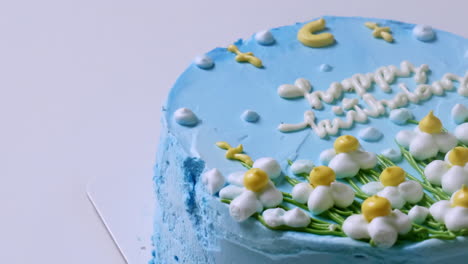 primer plano de la parte superior de un pastel de cumpleaños con glaseado azul y decorado con flores blancas y amarillas, con felicitaciones de cumpleaños en la parte superior