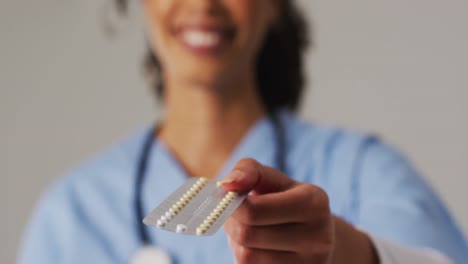 video of smiling biracial female doctor with pills on blue background