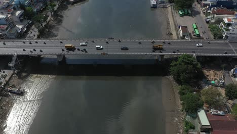 Drone-flight-along-Kenh-Te-canal-in-Ho-Chi-Minh-City-Vietnam-on-sunny-afternoon-with-river-boats,-waterfront-houses,high-rise-buildings-and-reflections