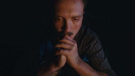 pensive man by firelight in darkness