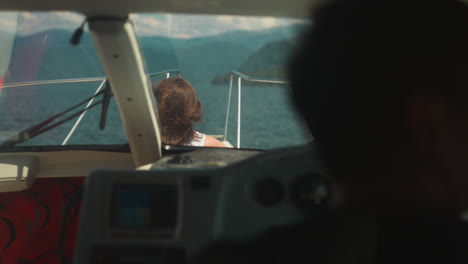 woman sits on deck while skipper controls motorboat in sea bay. lady enjoys water trip with professional yachtsman on summer vacation. seaside cruise