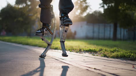 person on spring stilts walking on paved path in sunny park, captured from low angle focusing on legs in dark pants. scene highlights dynamic movement, vibrant energy, and natural outdoor