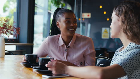 Dos-Jóvenes-Amigas-Reuniéndose-Y-Hablando-En-Una-Cafetería.