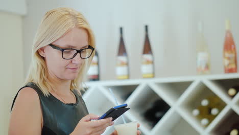 young woman in elegant black dress uses a smartphone in the tasting room of the winery