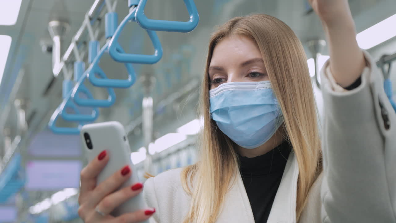 Woman using phone on public transportation wearing a mask.
