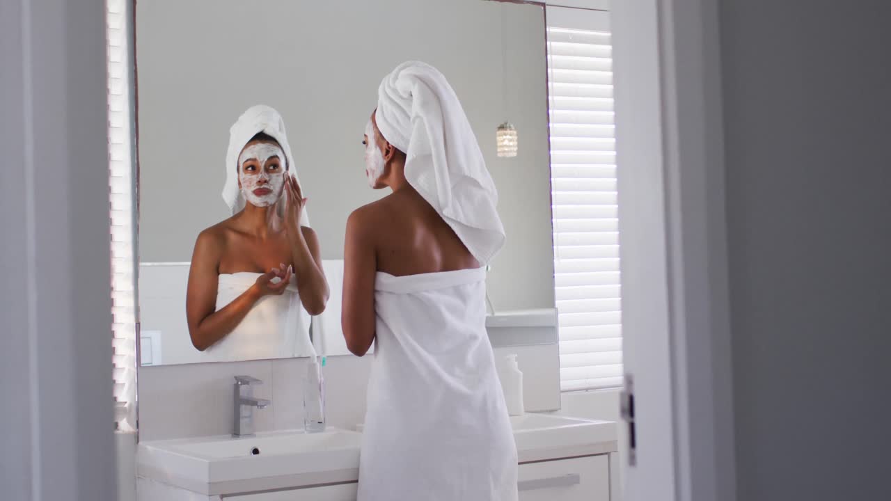 African american woman applying face mask while in the mirror at bathroom