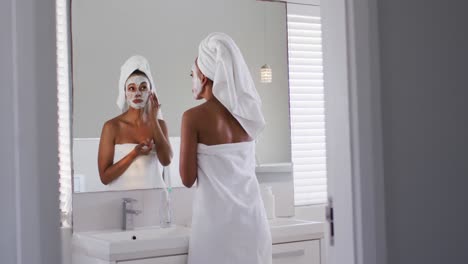 African-american-woman-applying-face-mask-while-in-the-mirror-at-bathroom