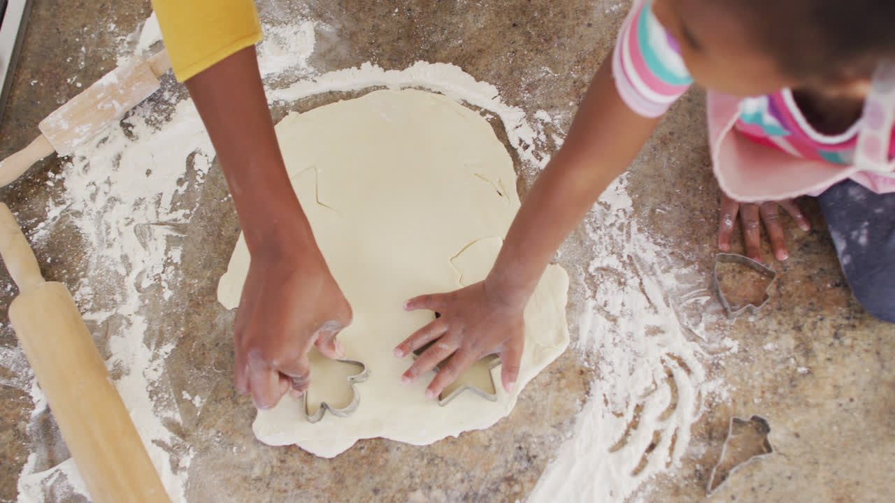 African american mother and daughter using cookie cutters in kitchen