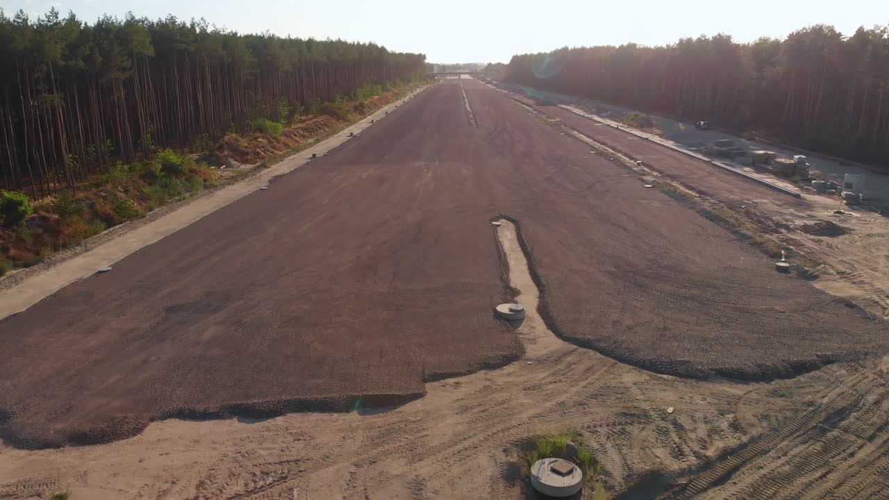 Aerial fly over highway construction site at sunset