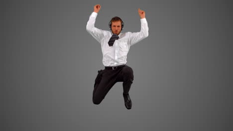 businessman jumping and listening to music on headphones on grey background